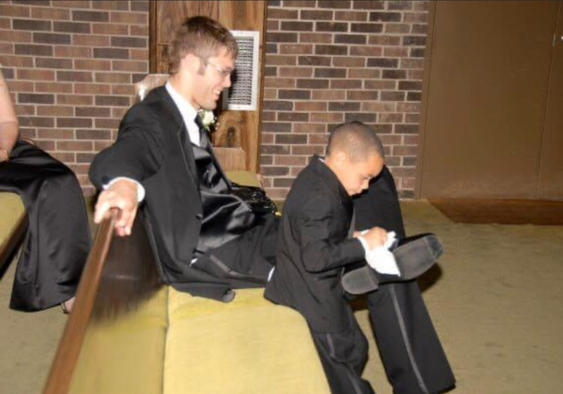 Picture of small boy shining shoes of man both in tuxes.